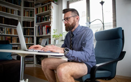 Zeigt im Homeoffice arbeitenden Mann in Shorts vor seinem Laptop