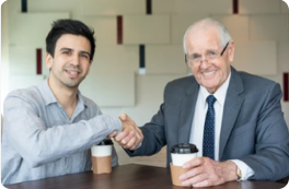 Junger und älterer Mitarbeiter schütteln sich die Hand (Symbolbild)